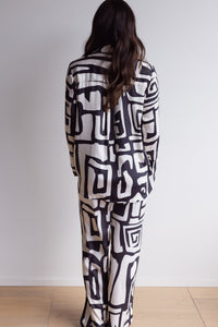 Woman from behind wearing silky, breathable 100% bamboo PJ set showing a long sleeve pyjama top and pants, both with a relaxed fit. With a bold geometric print in black and cream.