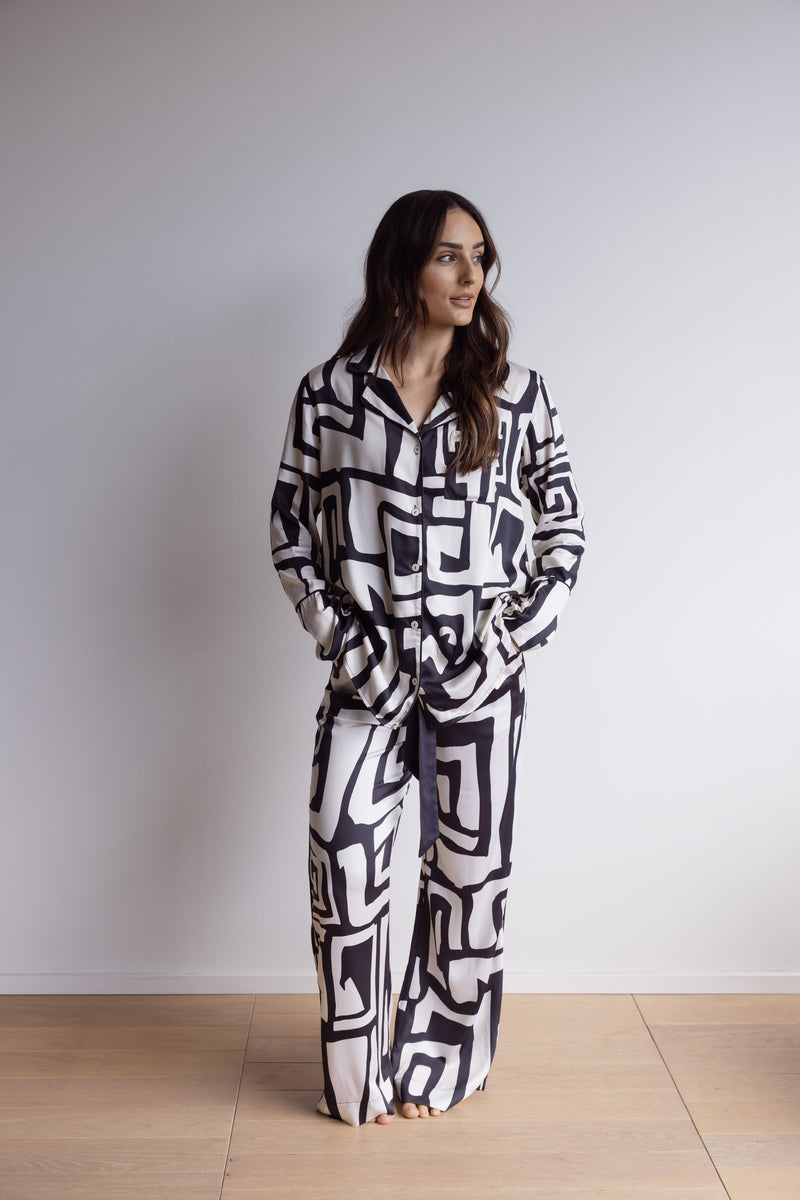 Woman wearing silky, breathable 100% bamboo PJ set showing a long sleeve pyjama top with button up design, pants with pockets and bold geometric print in black and cream.