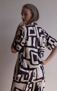 Woman looking over her shoulder wearing a short sleeve pyjama top and pants made of silky bamboo, with a bold geometric print in black and cream colour.