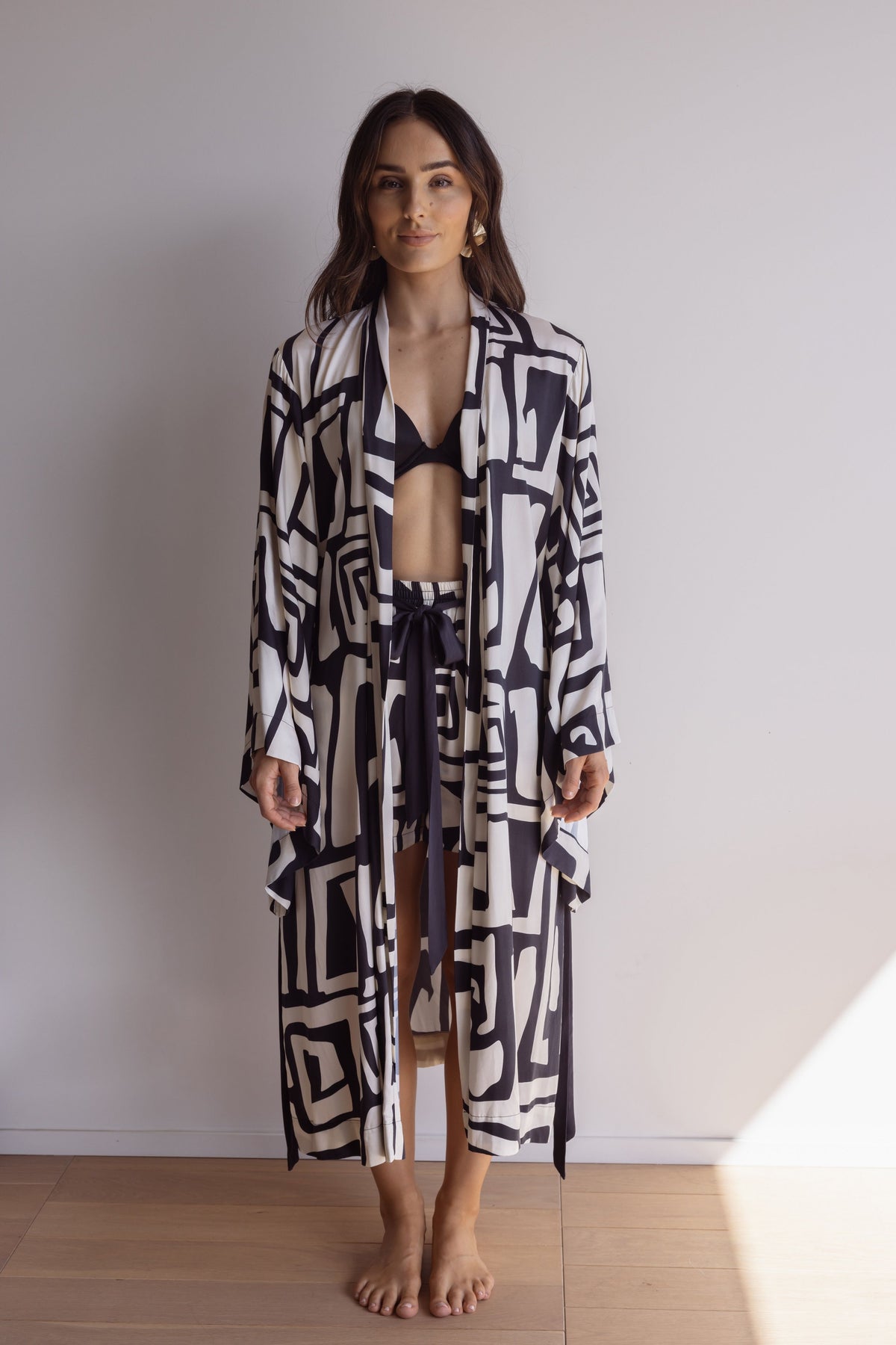 Woman wearing a lightweight, comfortable kimono-style robe. Made from silky-soft, breathable bamboo. Featuring a unique print design and a tie waist for an adjustable fit and hidden pockets. Perfect for relaxing.