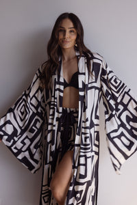 Woman wearing a kimono-style robe. Made from silky-soft bamboo with a flowing fit, featuring a unique print design and a tie waist for an adjustable fit. Hidden pockets and wide sleeves for a beautiful yet dramatic design. Perfect for lounging.