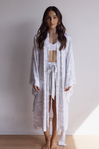 Woman wearing a comfortable kimono-style robe. Made from silky-soft, breathable bamboo. Featuring a unique print design and a tie waist for an adjustable fit and hidden pockets. Perfect for relaxing.