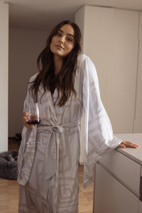 Woman wearing a comfortable kimono-style robe, made from silky-soft, breathable bamboo with a flowing fit, featuring a unique print design in grey and white. Tie waist for an adjustable fit and hidden pockets. Perfect for relaxing.