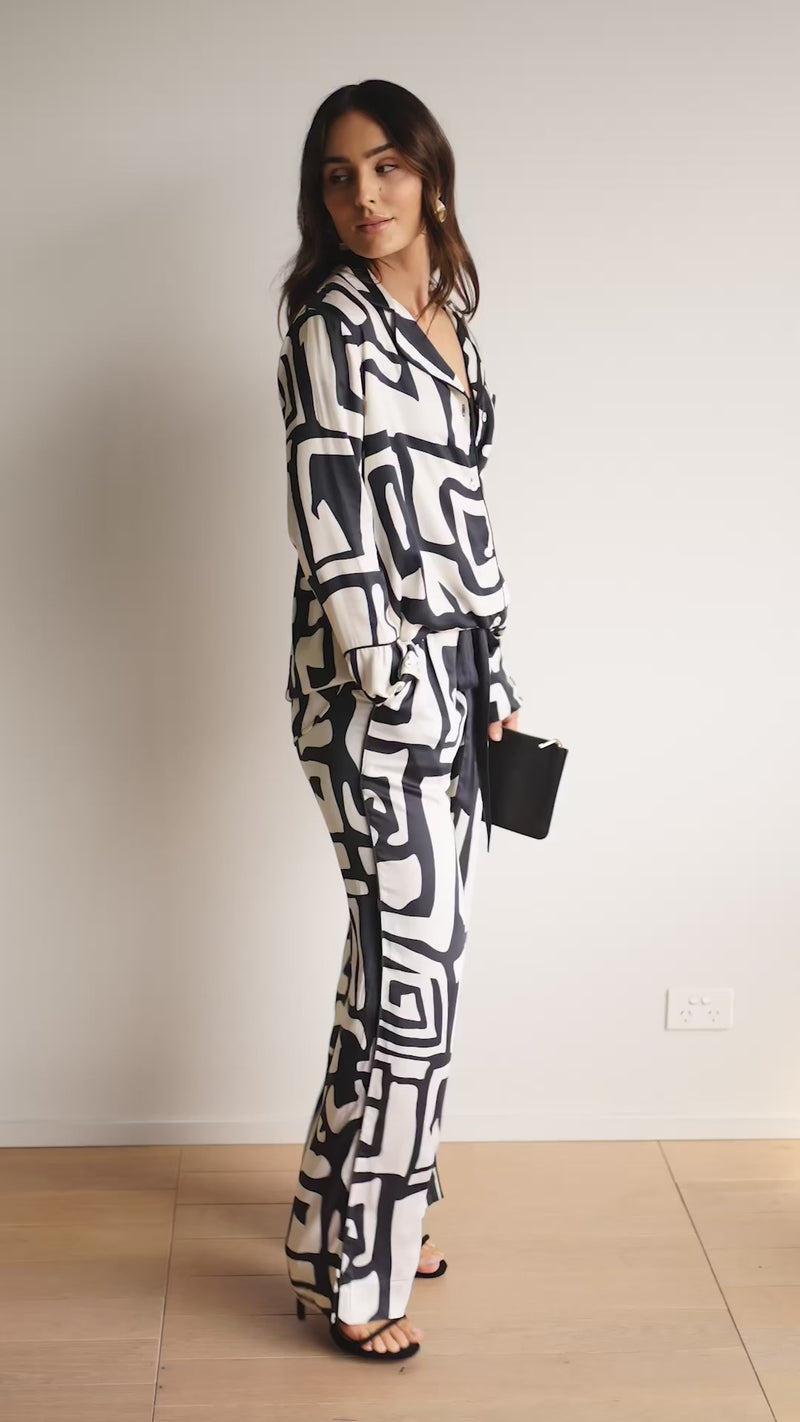 Woman wearing a luxurious long pyjama set made from ultra-soft bamboo, featuring a long-sleeve button-up shirt and matching pants. In a bold geometric print.